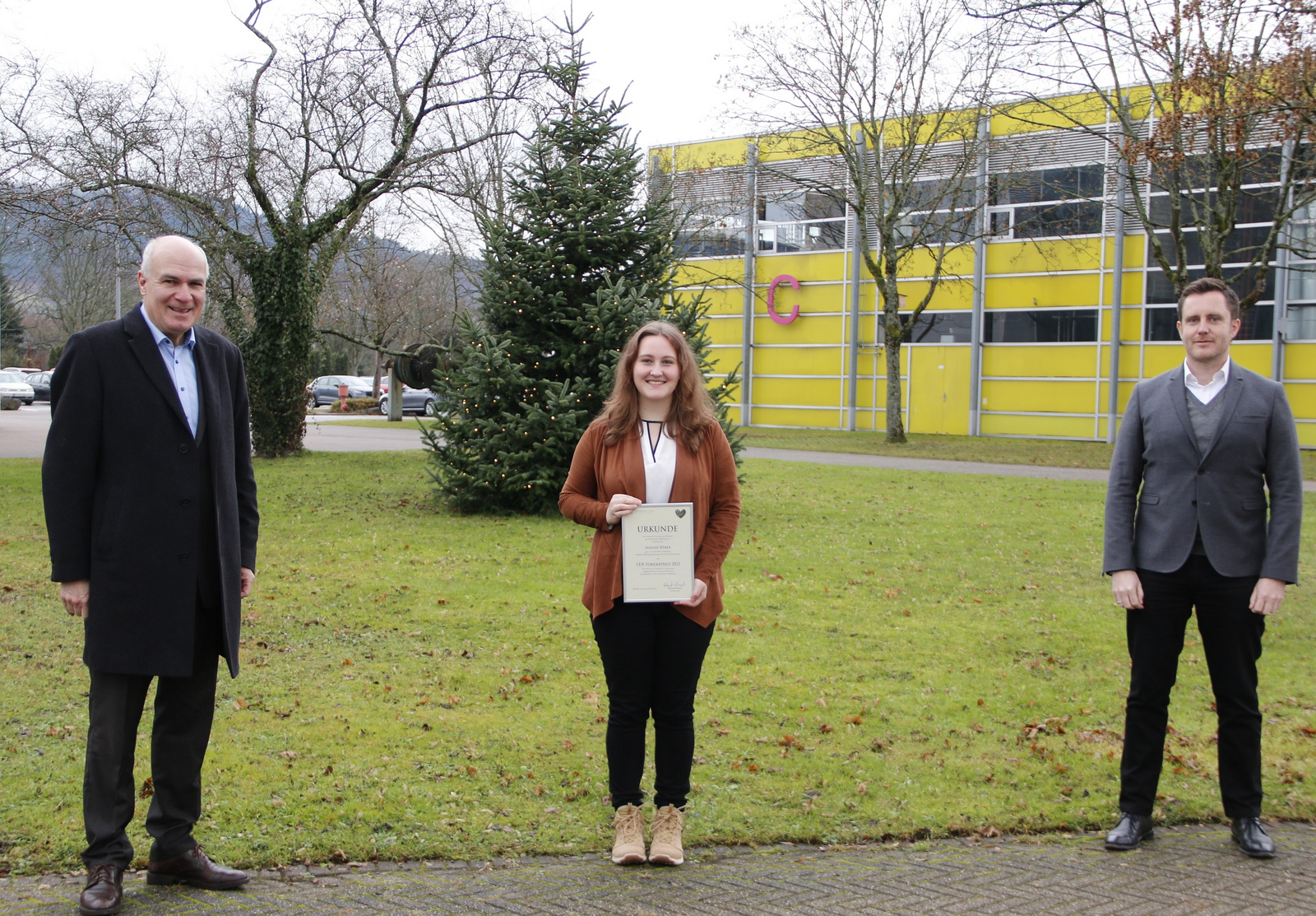 Der VdF-Vorsitzende Helmut Schareck, Nadine Weber und Prorektor Prof. Dr. Oliver Schäfer (von links) stehen auf dem Campus vor einem Weihnachtsbaum.